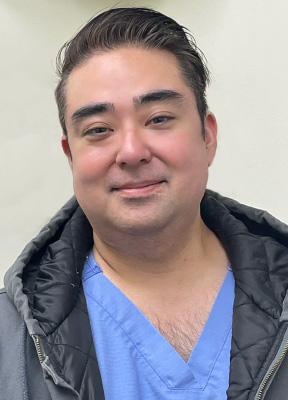 A man in a blue surgical scrubs, smiling at the camera.