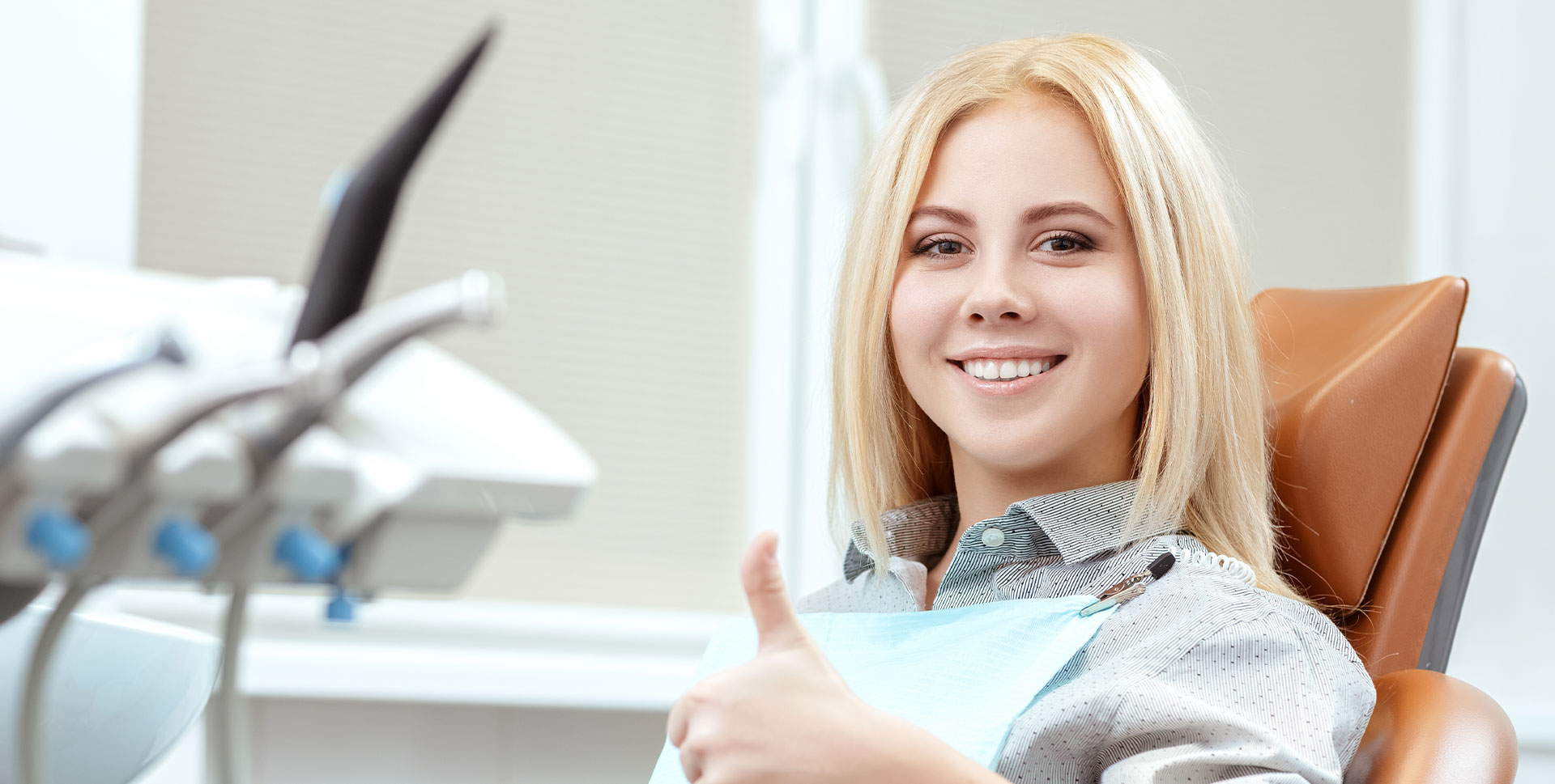 A woman in a dental office, smiling and giving a thumbs-up.