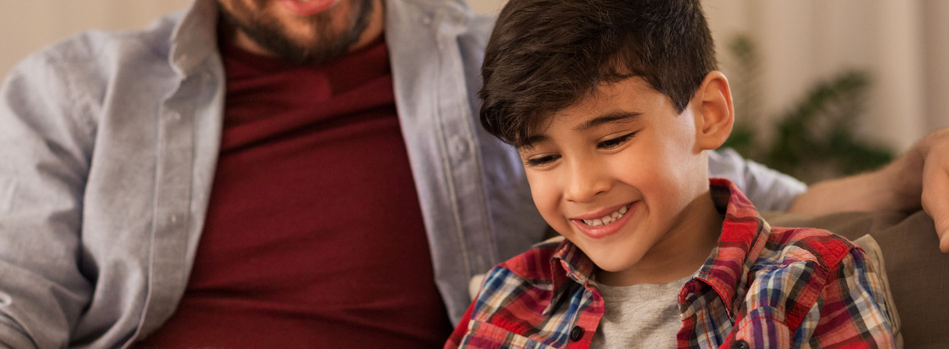 A man and a young boy are seated closely together, smiling and looking at something off-camera.