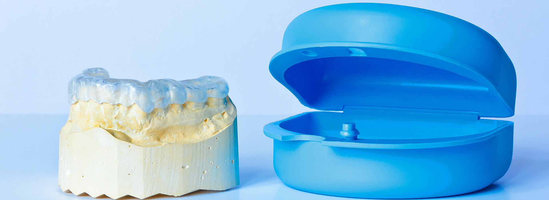 The image shows a transparent dental model on the left and a blue, plastic mouthguard on the right.