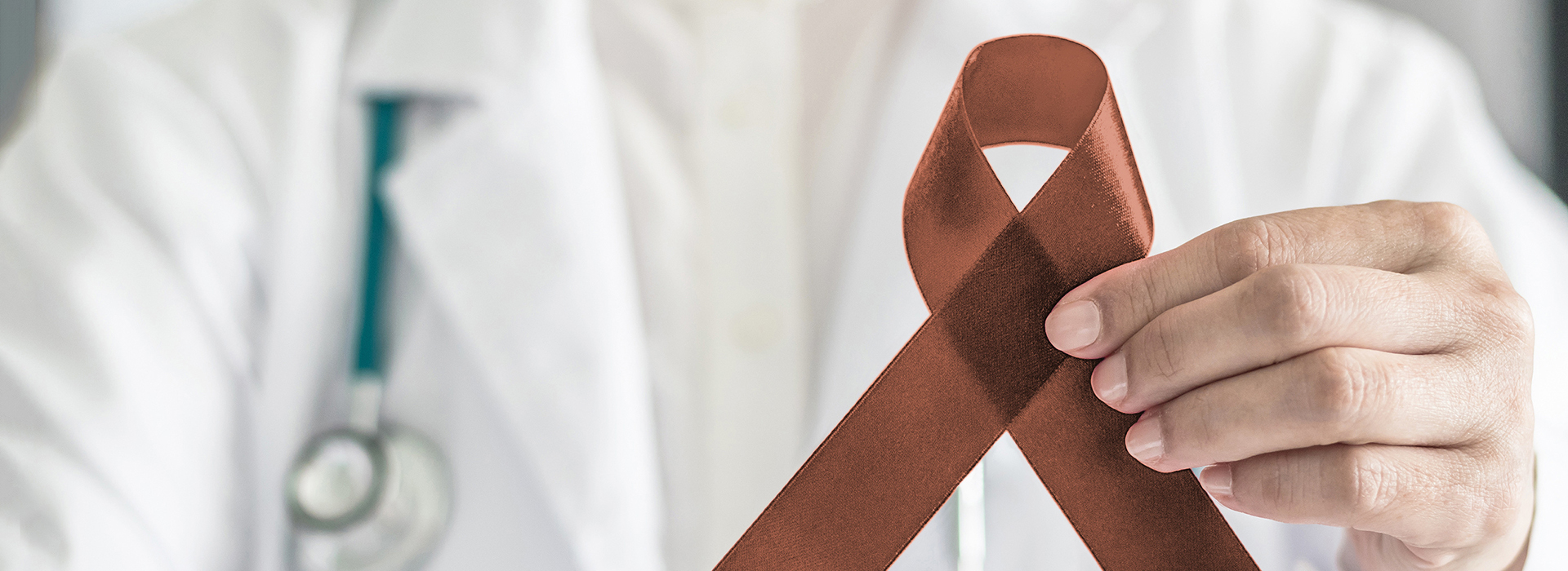 The image features a person in a white lab coat holding a brown ribbon with a red symbol on it.