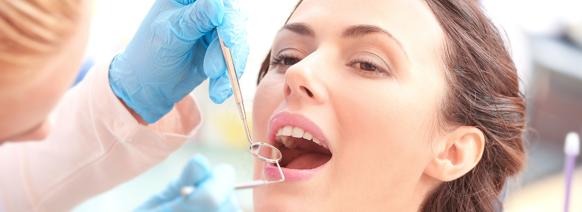 The image shows a woman receiving dental care, with a dentist performing a procedure on her teeth using specialized equipment.