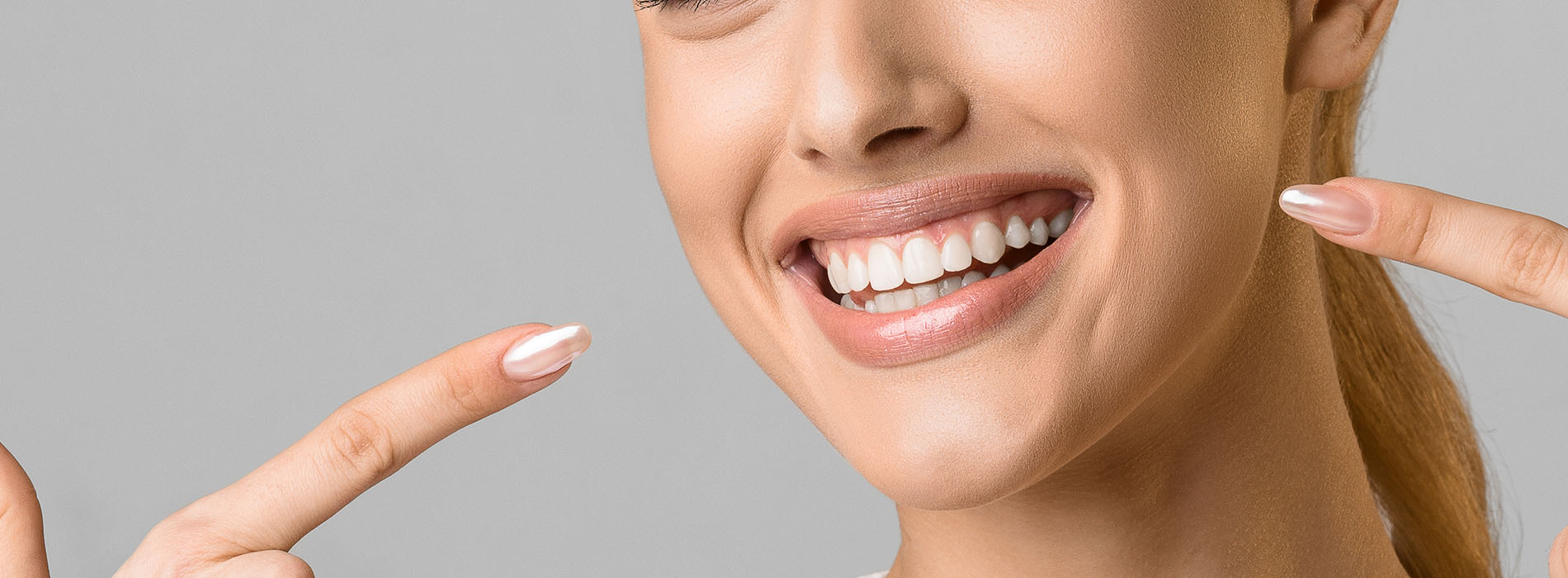 A woman with a radiant smile, holding up fingers near her face, against a neutral background.