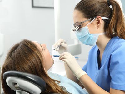 The image depicts a dental hygiene professional performing a cleaning or examination on a patient in a dental office setting.