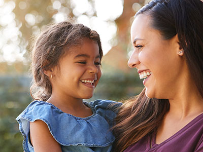 A woman and a young girl smiling at the camera, with the woman holding the child in her arms.