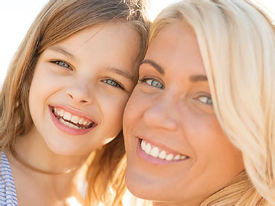 A smiling woman and a young girl posing for a photo, with the woman s face partially obscured by the child s head.