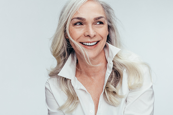 A woman with short hair, wearing a white top, smiling and looking to the side.