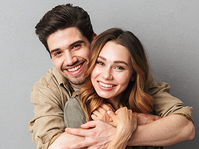 A young couple embracing in a warm hug, both smiling and looking content.