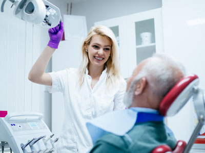 A dental hygienist is assisting an elderly man with a medical device in a dental office setting.