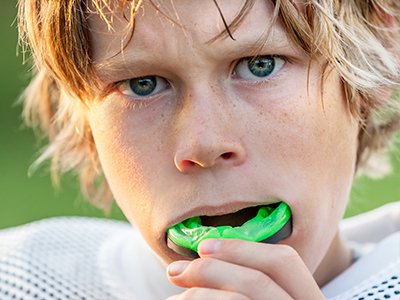 A young boy with a green toothbrush in his mouth, looking directly at the camera.