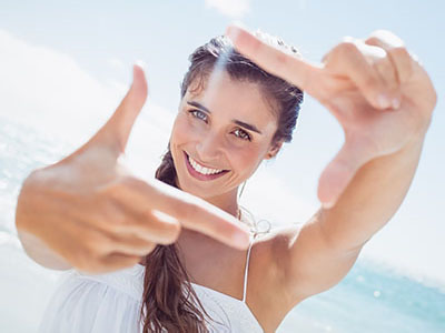 A young woman with long hair is smiling and holding up a peace sign with her right hand.